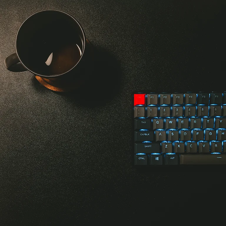 backlit gaming keyboard with a mug of black coffee